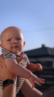 Dikey video. Genç baba kucağına alır ve kulübesinin arka bahçesinde tatlı bir çocuğu öper. Sakallı adam, kırsal kesimde havadaki sevimli oğlunu yetiştirme oyunu oynuyor. Babalığın mutlu anları