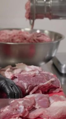 Aşçı, üretim tesisinin mutfağında et kesmek için bıçak kullanıyor. Dar eldivenlerde uzman et parçaları oluşturur ve doğranmış nesneleri dikey görüntülemek için öğütücü uygulamaya hazırlanır.