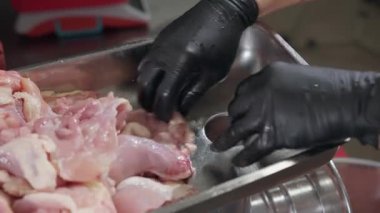 Aşçı elleri, tavuk parçalarını elektrikli et öğütücüsünün işlem bölümüne yerleştirir. İşçi, yarı bitmiş ürünler yaratmak için özel mutfak gereçleri ve eldivenler kullanır.
