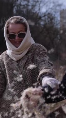 Zarif giyinmiş gülümseyen son sınıf öğrencisi arkadaşlarıyla sonbahar parkında dikey çekimde kuru kedi kuyruğu tüylerini sallıyor. Sevgili kocasıyla birlikte olgun bir kadın nehir kıyısında 