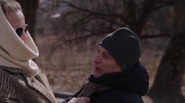 Olgun bir eş sevilen kocanın şapkasını ve eşarbını bahar parkında düzeltir. Kıdemli kadın, romantik partnerinin şehir sonbahar bahçesinde birlikte vakit geçirmesini benimsiyor. Mutlu evlilik sırrı.