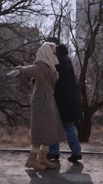 Dikey video. Son sınıfların mutlu çifti bahar parkında dirseklerini birleştiriyor. Mutlu olgun kadın ve erkek, aşk ilişkisinin mutluluğunu şehir sokaklarında paylaşarak dans ediyor. Evlilik yıldönümü