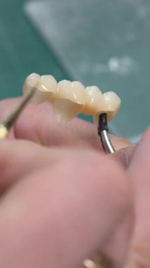 Teknisyen eli, diş implantı kapaklarına boya sürerek laboratuvarda doğal gölgeler yaratıyor. Ortodontist renkleri diş köprüsü diş minesi ile stomatolojik klinikte dikey video fırçası