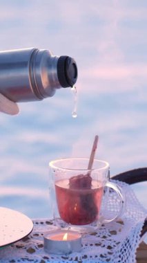 Kışın açık havada vakum tüpünden çay bardağına sıcak su döker. Turist, kamp videosunda naneli ve limonlu lezzetli sıcak vitamin içeceği hazırlıyor.