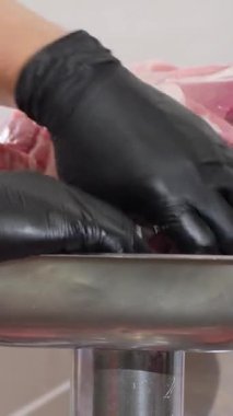 Dikey video. Uzman, et parçalarını öğütmek için özel bölmelere yerleştiriyor. Dar eldivenli bayan aşçı, üretim atölyesinde kıyma yapmak için özel kıyma makinesi kullanmaya hazırlanıyor.