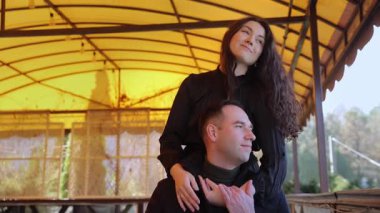 Genç bir kadın erkek arkadaşını açık hava restoranının terasında öpüyor ve sarılıyor. Mutlu romantik çift bahar günü çardakta tutkulu duygular ifade eder. Sevgi dolu bir ilişki