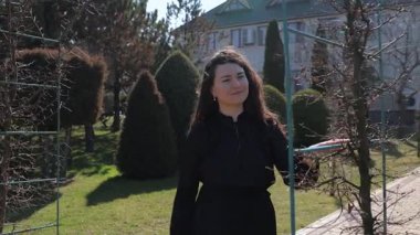 Siyah giysili mutlu esmer kadın güneşli bahar parkındaki genç ağaç dallarına bakıyor. Güzel bayan yeşil bahçede yürürken çıplak dallara dokunuyor. İlkbahar atmosferi