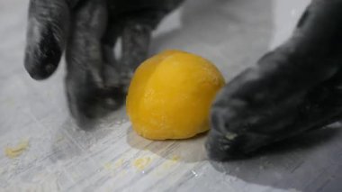 Fırıncı elleri şekle girer ve pastaneye yakın çekimde mango mochi kekine pudra şekeri ekler. Profesyonel şekerci Japon tatlısını mutfakta tropikal meyvelerle süslüyor. Sağlıklı tatlılar