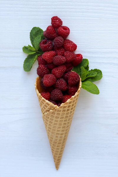 Raspberry in waffle cone on white wooden table. Delicious raspberry.