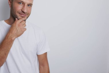 Düşünceli bir adam beyaz arka planda çenesine dokunuyor.