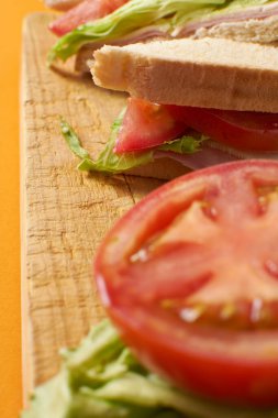 Turuncu arka planda domates ve marullu sağlıklı jambonlu ve peynirli sandviç.