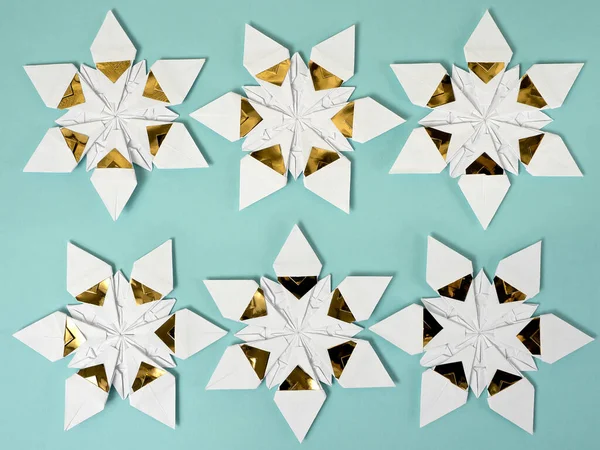 Beyaz ve altın folyo kağıtta iki sıra halinde altı origami yıldızı soluk mavi kağıt arka planda
