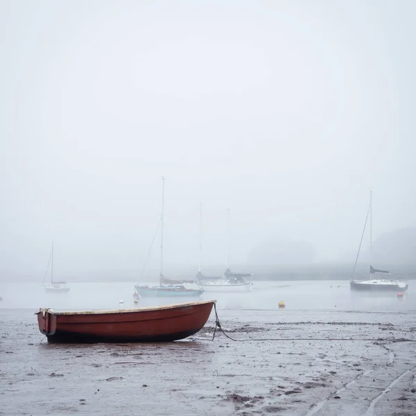 Small boats moored on the estuary at low tide as the fog rolls in