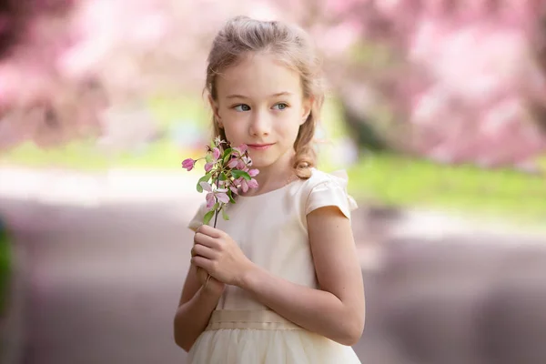 Cute little girl smiles and sniffs flowers in a spring blooming garden, close up — Stock Photo, Image
