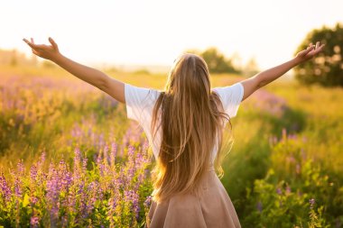 Gün batımında mor bir alanda gülümseyen mutlu kadın, özgürlük kavramı.