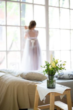 Mutlu genç bir kadın güneşli bir sabahın tadını çıkarır. Kız pencereden dışarı bakıyor. Masanın üzerinde bir buket çiçek var..