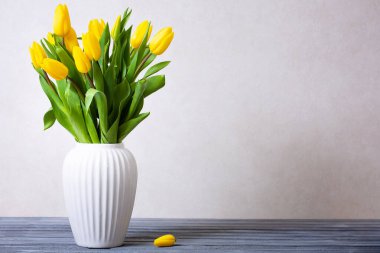 Beyaz vazoda sarı laleler açık gri arka planda masanın üzerinde. İlkbahar