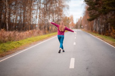 Kırsal kesimde boş yolda yürüyen bir kadın. Macera, spor, egzersiz, özgürlük ve hareket.