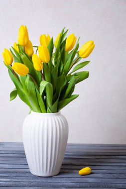 Beyaz vazoda sarı laleler açık gri arka planda masanın üzerinde. İlkbahar