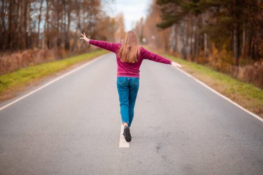 Kırsal kesimde boş yolda yürüyen bir kadın. Macera, spor, egzersiz, özgürlük ve hareket.