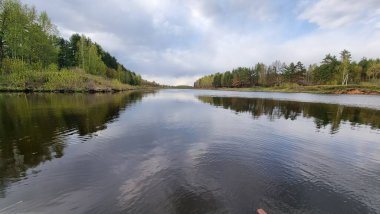 Nehir kırsal alanda esiyor. Nehir kıyıları ağaçlar, çalılar ve tarlalardan oluşur ve uzaklardan demirli bir tekne görülebilir..