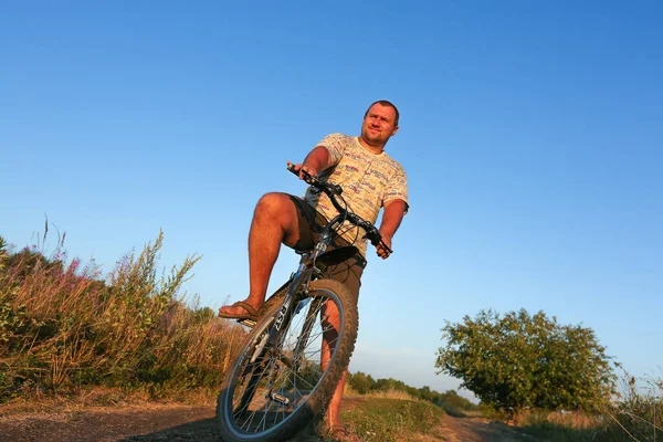 An adult rides a bicycle through the countryside and the forest by the river. Outdoor sports. Bicyclist at sunset. Cycling activity of a tourist who has fun doing outdoor sports.