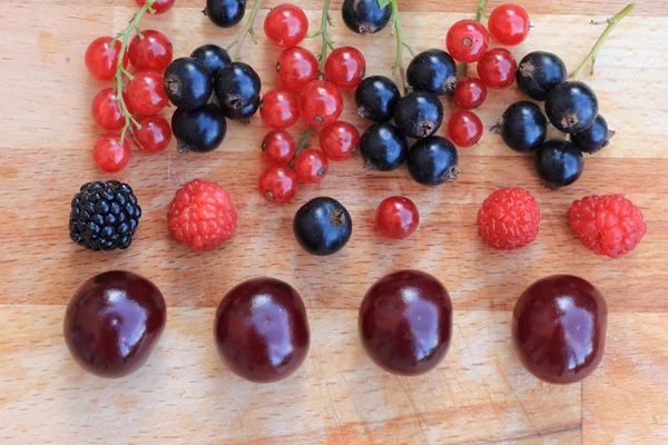 Berries red and black currants, raspberries, blackberries and cherries closeup on a wooden table — Stock Photo, Image