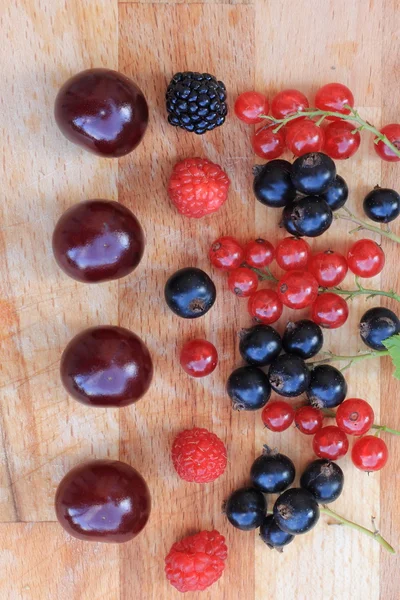 Rote und schwarze Johannisbeeren, Himbeeren, Brombeeren und Kirschen in Großaufnahme auf einem Holztisch — Stockfoto