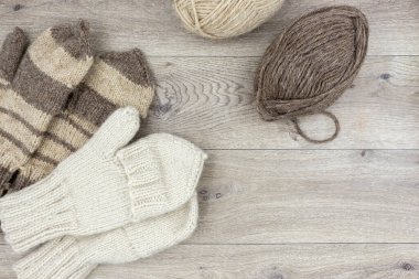 Ahşap arka planda iplik derileri ve örgü eldivenler. Kapaklı eldivenler. Hobi, ev yapımı ve bireysel girişimcilik kavramı.