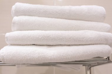 Otel banyosunun rafında bir yığın temiz beyaz havlu duruyor.