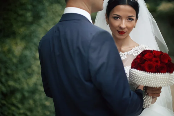 Braut umarmt Bräutigam und hält Blumenstrauß — Stockfoto