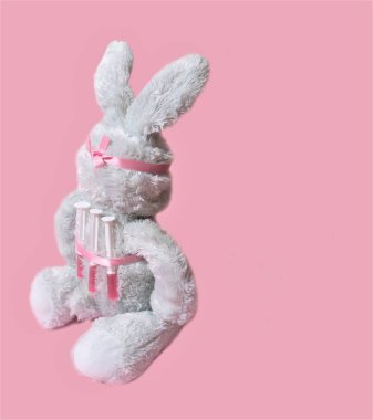 Açık gri Paskalya tavşanı. Üzerinde pastel pembe arka planda aşılar olan ninja Covid-19 virüsüyle savaşmak için yola çıktı..