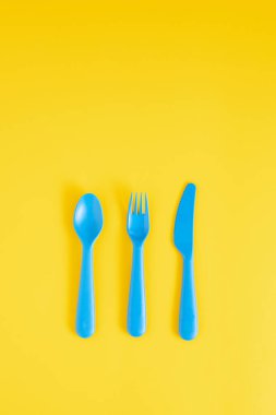 Mavi kaşık, çatal ve bıçak. Fotokopi alanı olan parlak sarı bir arka plan. Düz konsept yatıyordu.