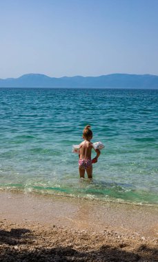 A young little girl is playing in the shallow water of the beautiful Adriatic Sea on the Croatian coast during family vacation. Summer holidays vibes.