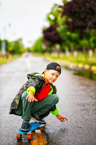 Teenager Čepici Zelené Bundy Jezdí Modrém Skateboardu Silnici — Stock fotografie