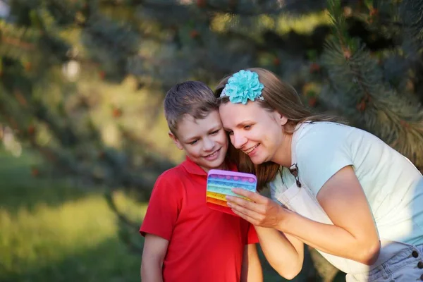 8 year old boy with his mom are playing with popit in the park. happy child with a toy. Son and mom in bright summer casual clothes