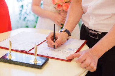 Gelin ve damadın elleri kayıt bürosunda yakın çekim evraklarını imzalar..