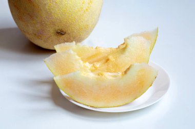 Beyaz bir tabakta dilimlenmiş taze kavunlar beyaz bir masada yatıyor.