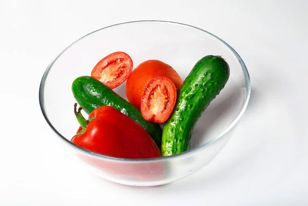 Tomates fraîches, concombres et poivrons rouges dans un bol transparent isolé sur blanc. — Photo