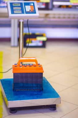 Araba aküsü, bulanık bir rafın arka planında zemin terazisinde duruyor..