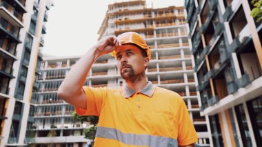 İnşaat işçisi, şantiyede kaskını takıyor. Önce güvenlik, meslek anlayışı. İnşaatçı sert şapka üniformasını giyer ve işe hazırlanır. Adam turuncu kapaklı şantiye yapıyor..