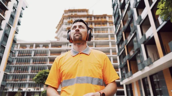 安全装備の補聴器を身に着けている男 イヤーディフェンダーやイヤーマフをキャンセルするノイズを身に着けている労働者 建設業者はヘッドフォンで耳を保護します 仕事中の安全管理 — ストック写真