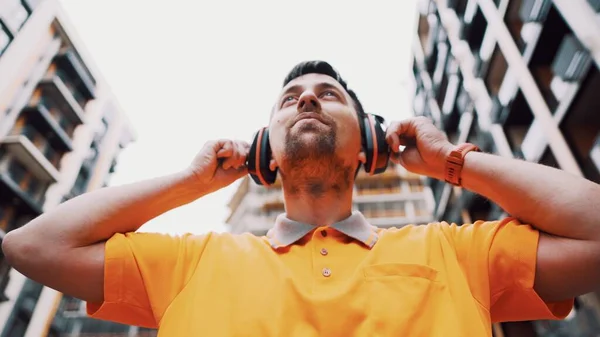 Man wearing safety equipment hearing protection. Worker wearing noise cancelling ear defenders or ear muffs. Construction builder puts on protect ears with headphones. Taking care safety during work.