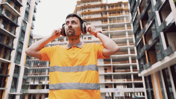 建設現場で働いている耳のマフを持つ建設労働者 労働者は耳の守備を音から守るために置く 健康管理 職場の安全管理 耳栓だ 音がうるさくて聞こえが悪い — ストック写真