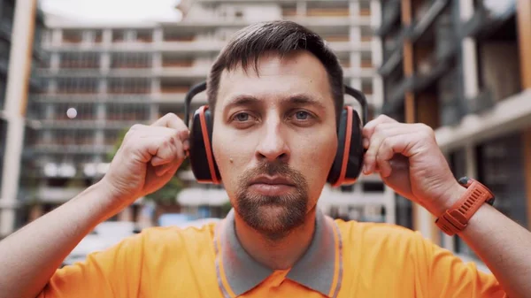 Man wearing safety equipment hearing protection. Worker wearing noise cancelling ear defenders or ear muffs. Construction builder puts on protect ears with headphones. Taking care safety during work.