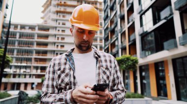 Mobil uygulamaların geliştirme yönetim sürecine dahil edilmesi. İnşaat sahasındaki cep telefonunda sabit şapka kullanan beyaz mühendis inşaat projesini kontrol eden mühendis..