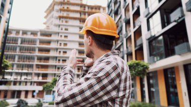 Mühendis telefonda konuşuyor. İnşaat alanında telefonu kullanan bir mimar. Foreman 'ın telefon kontrol işlemleri. İnşaat sektöründe inşaat işçisi iletişimi. Profesyonel telefon binası.