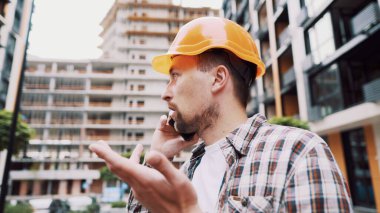 Mühendis telefonda konuşuyor. İnşaat alanında telefonu kullanan bir mimar. Foreman 'ın telefon kontrol işlemleri. İnşaat sektöründe inşaat işçisi iletişimi. Profesyonel telefon binası.