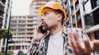 Mühendis telefonda konuşuyor. İnşaat alanında telefonu kullanan bir mimar. Foreman 'ın telefon kontrol işlemleri. İnşaat sektöründe inşaat işçisi iletişimi. Profesyonel telefon binası.