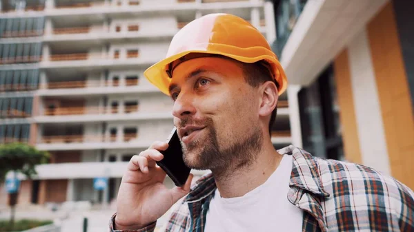 Mühendis telefonda konuşuyor. İnşaat alanında telefonu kullanan bir mimar. Foreman 'ın telefon kontrol işlemleri. İnşaat sektöründe inşaat işçisi iletişimi. Profesyonel telefon binası.